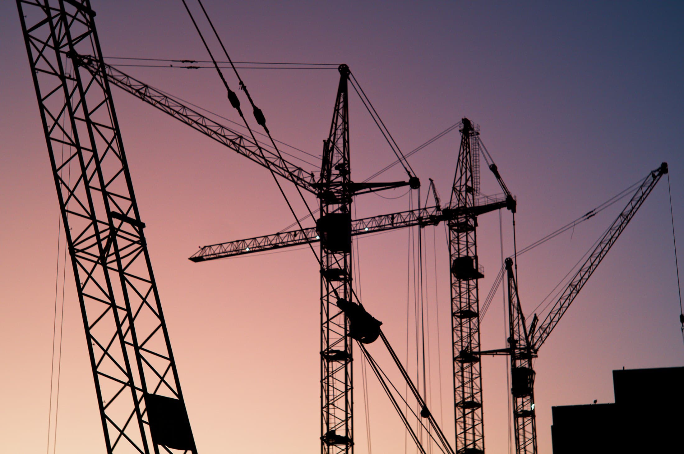 Tower cranes silhouetted against the evening sky